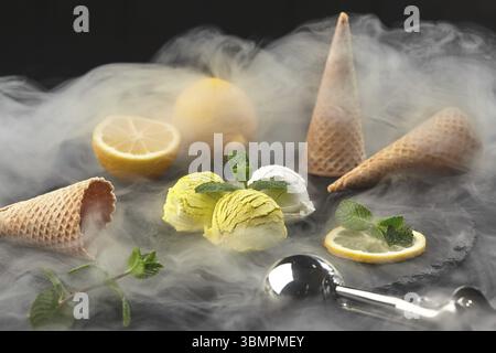 Nahaufnahme eines natürlichen, köstlichen Creme- und Zitroneneis, dekoriert mit frischer Minze und serviert in Rauch auf einem dunklen Steinschiefer auf einem schwarzen Rücken Stockfoto