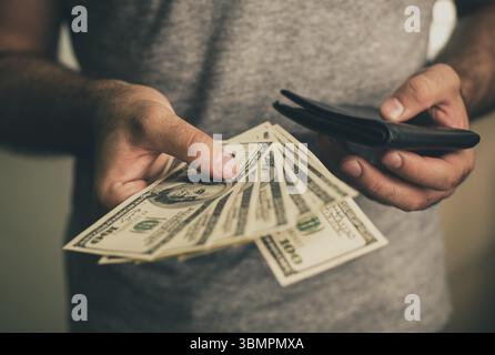Ein Mann in einem grauen T-Shirt hält Dollar und schwarze Brieftasche in der Hand. Bank. Kasino. Gehalt. Preise Stockfoto