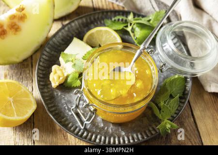 Süße Melonen- und Zitrusmarmelade oder Gelee in einem kleinen Glas mit frischen Melonenscheiben auf rustikalem Holztisch. Hausgemachtes Preserve Stockfoto