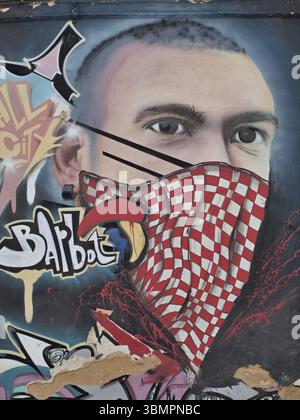 Urbane Kunst eines Mannes, der ein rot-weiß kariertes Bandana trägt, das den unteren Teil seines Gesichts bedeckt und mit Sprühfarbe auf einer verwitterten Wand hergestellt wurde Stockfoto
