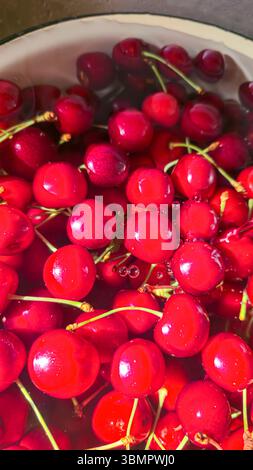 Große Kirschen in einer großen Schüssel in Wasser. Wasser fließt, Obst vor dem Essen waschen. Vitamine Stockfoto