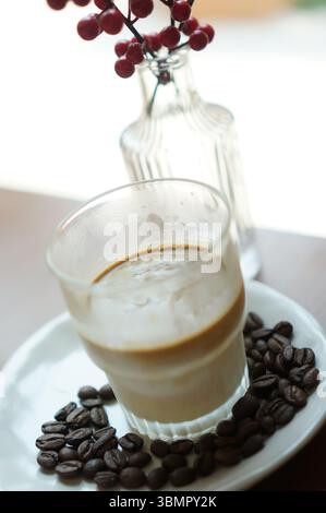 Ein Glas Kaffee mit ein paar Kaffeebohnen auf einem weißen Teller Stockfoto