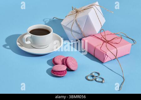 Valentinstag Grusskarten. Weiß Kaffeetasse, Rosa Makronen und Geschenkboxen auf blauem Hintergrund. Ansicht von oben mit der Kopie. Immer noch leben. Flach Stockfoto