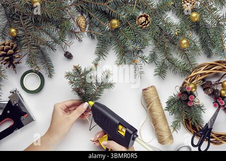 Blick von oben auf die weibliche Hände machen Weihnachten ein Kranz. Verpackt Geschenke und blättert, fichte Äste und Tools auf weißer Tisch. Vorbereitung auf Weihnachten oder Y Stockfoto