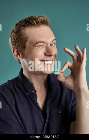 Nahaufnahme Porträt einer jungen schönen Ingwer Person nür für diese in einem stilvollen Navy t-shirt, das OK-Zeichen, Blick in die Kamera lächeln und posieren, während auf Blau stu Stockfoto
