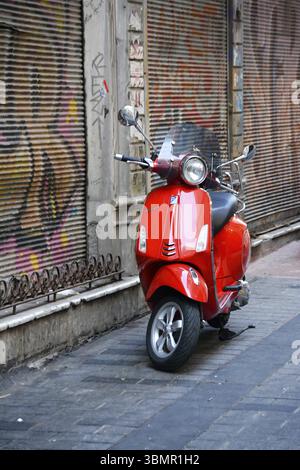 Glänzend rote Vespa parkte auf einem Bürgersteig vor einer farbenfrohen Graffiti-Wand Stockfoto