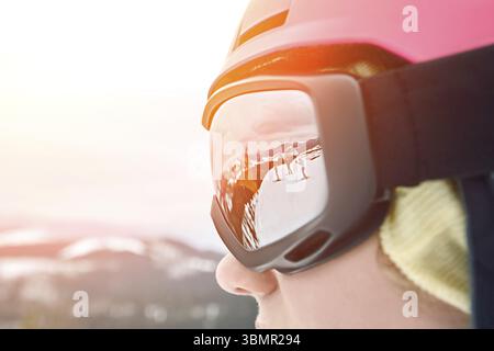 Nahaufnahme des Porträts einer Snowboarderin im Skigebiet, die Helm und Schutzbrille trägt, die Berge reflektiert, und eines anderen Snowboarders oder Skifahrers und Skifahrers Stockfoto