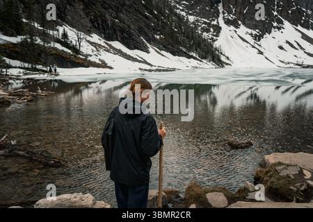 Die junge Frau schaut mit Reflexion in den teilweise gefrorenen Alpensee Stockfoto