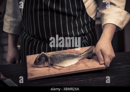 Koch schneidet den Fisch auf einem Brett. Foto in Brauntönen. Küche. Holztisch Stockfoto