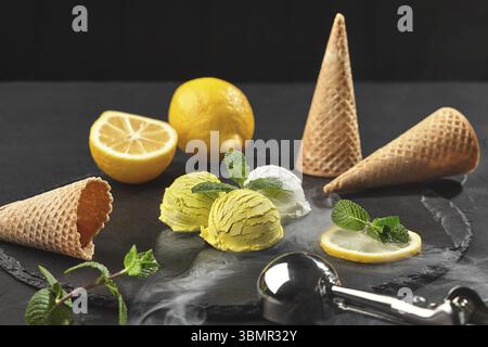 Nahaufnahme eines natürlichen aromatischen Creme- und Zitroneneises, dekoriert mit frischer Minze und serviert in Rauch auf einem Steinschiefer auf schwarzem Hintergrund Stockfoto