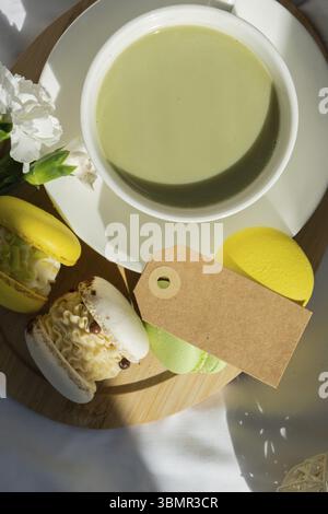 Papiernotiz Kopie Raum Vorlage Süße gelbe Macaron Dessert Tasse grüner pflanzlicher Matcha Tee Latte in gemütlicher Morgenbettatmosphäre. Kreativer Urlaub Stockfoto