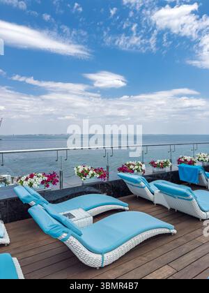 Entspannungsbereich mit modernen weißen und blauen Chaiselongues auf einer Terrasse mit Panoramablick auf das Meer. Perfekter Sommer für Reisen und Freizeit Stockfoto