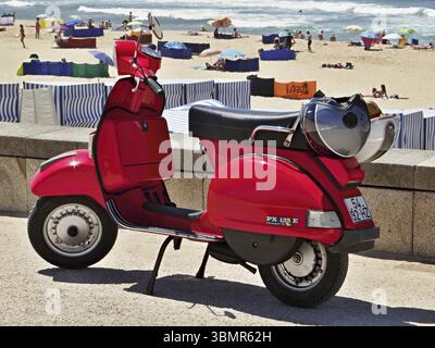 Die glänzend rote Vespa Piaggio parkte in der Nähe eines Strandes voller Touristen, die Sommerferien genießen Stockfoto