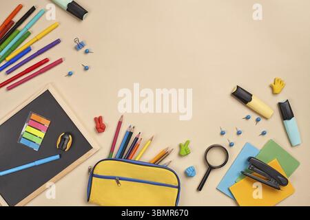 Helles, flaches Foto eines Arbeitsplatzes mit Schulzubehör, wie drei Markierungen, farbige Bleistifte, gelbe Bleistiftetui, Filzstifte, Lupe Stockfoto
