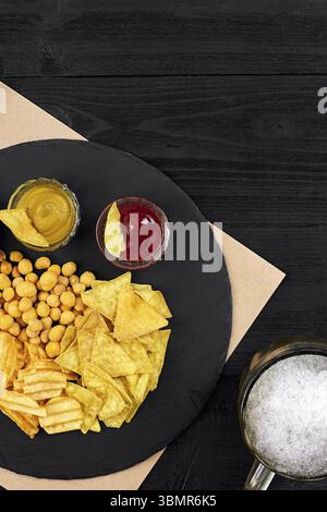 Blick von oben auf Bierglas und Snacks mit Sauce auf schwarzem Holztisch. Draufsicht. Speicherplatz kopieren. Stillleben. Flach liegend Stockfoto