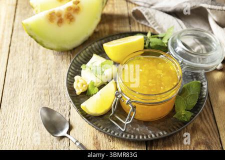 Hausgemachtes Preserve. Süße Melonen- und Zitrusmarmelade oder Gelee in einem kleinen Glas mit frischen Melonenscheiben auf rustikalem Holztisch. Kopierbereich Stockfoto