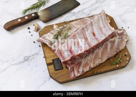 Rohe Kalbskalbsbrust Rippchen Fleisch mit Rosmarin und Gewürzen auf kurzen Ersatzrippchen zum Kochen auf Marmorplatte Stockfoto