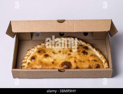 Geschlossene Pizza-Calzone in Packbox auf grauem Hintergrund Stockfoto