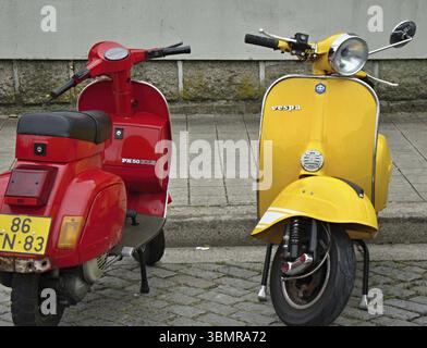 Zwei farbenfrohe Vespa-Roller parken auf einer kopfsteingepflasterten Straße mit klassischem italienischem Design Stockfoto