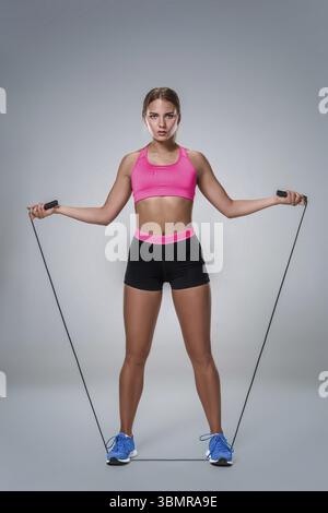 Volle Länge Bild eines hübschen Fitness Frau tun Übung mit Springseil über grauen Hintergrund. Junge Frau mit schönen schlanken gesunden Körper posin Stockfoto