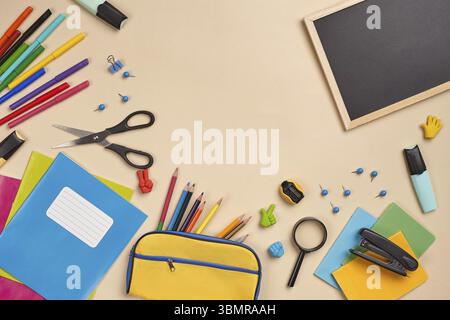 Helles flaches Lay-Foto eines Arbeitsplatzes mit Schulunterlagen, wie drei Markierungen, farbigen Bleistiften, gelbem Bleistiftetui, Filzstiften, Lupe Stockfoto