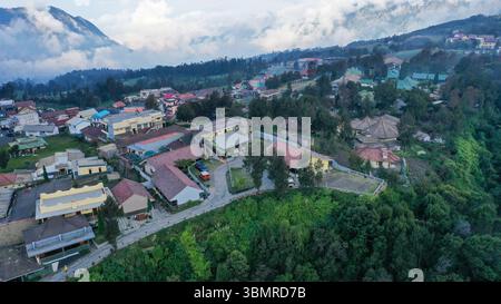 Der Blick aus der Vogelperspektive auf Cemoro Lawang zeigt farbenfrohe Dächer an einem Berghang, umgeben von nebeligen Wäldern und sanften Hügeln, die einen ruhigen Hi schaffen Stockfoto