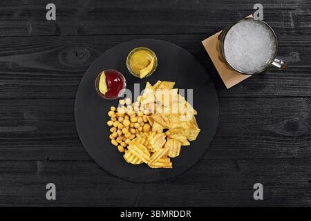Blick von oben auf Bierglas und Snacks mit Sauce auf schwarzem Holztisch. Draufsicht. Speicherplatz kopieren. Stillleben. Flach liegend Stockfoto