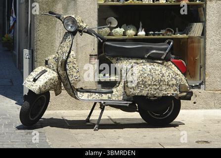 Geparkter, maßgeschneiderter Vespa-Roller mit Muscheln, die das Äußere bedecken, auf einem Bürgersteig vor einer Ladenfront in Portugal Stockfoto
