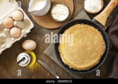Wir feiern den Pfannkuchen-Tag, kochen ein gesundes Frühstück. Köstliche hausgemachte Crepes oder Pfannkuchen in einer Pfanne und Zutaten auf einem rustikalen Tisch. Ansicht von Stockfoto