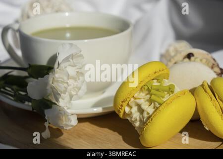 Süßes gelbes Macaron Dessert Tasse grüner Matcha Tee Latte auf Pflanzenbasis in gemütlicher Morgenliegenatmosphäre. Kreative Urlaubsidee mit romantischem Date. Pflanzliche Präparate Stockfoto