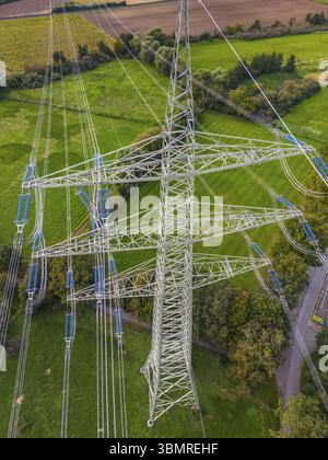Drohnenaufnahme aus Hochspannungspylon mit vielen Stromleitungen in grüner Natur als Konflikt zwischen Technologie und Zivilisation Stockfoto
