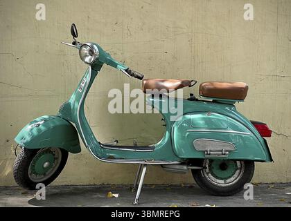 Ein grüner Vespa-Roller im Vintage-Stil, der vor einer verwitterten Wand geparkt ist, zeigt sein zeitloses Design und seinen Retro-Charme Stockfoto