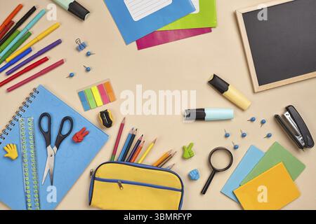 Helles, flaches Lay-Foto eines Arbeitsplatzes mit Schulunterlage, z. B. blauem Notizbuch, drei Markierungen, farbigen Bleistiften, gelbem Bleistiftetui, Filzspitze Stockfoto