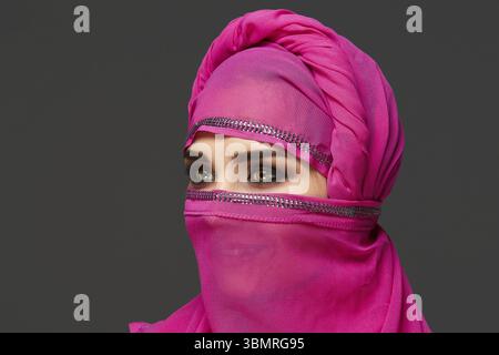 Nahaufnahme einer gut aussehenden jungen Frau mit ausdrucksstarken rauchigen Augen, die den schicken rosa Hijab trägt, der mit Pailletten verziert ist. Sie hat ihren Kopf gedreht Stockfoto