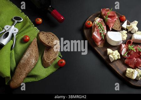 Flasche Wein mit Käse und traditionellen Würstchen auf Holzbrett auf schwarzen Hintergrund mit kopieren. Immer noch leben. Ansicht von oben. Flach Stockfoto