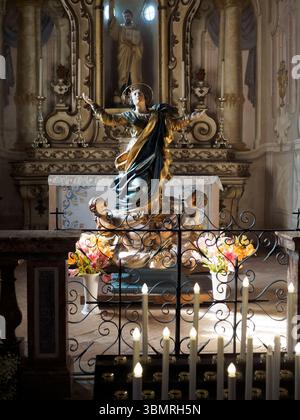 Alseno, Italien 22. Juni 2025 Goldene Jungfrau-Maria-Statue, die Schutzarme ausbreitet, darunter liegend, von Kerzenlicht in Chiaravall beleuchtet Stockfoto