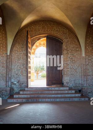 Alseno, Italien 22. Juni 2025 Sonneneinstrahlung durch Holztüren, beleuchtete Steinbögen und stille Kreuzgänge von Chiaravalle della Colomba Abbe Stockfoto
