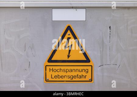 Gelbes Schild mit Warnung Hochspannungsgefahr auf Schaltkasten mit deutschem Text Stockfoto
