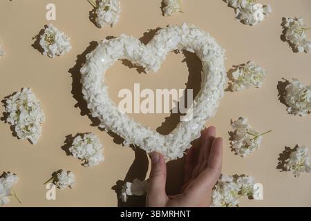 Frauenhandherz aus weißen Fliederblüten auf pastellbeigem Hintergrund. Stillleben romantische Komposition von Valentinstag Feiertag Kopierraum für Ihr Stockfoto