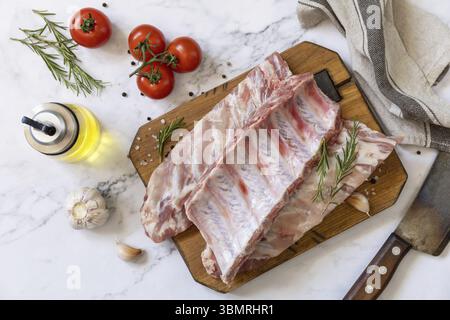 Rohe Kalbsbrust Rippchen Fleisch mit Gemüse und Gewürzen auf kurzen Ersatzrippchen zum Kochen auf Marmorplatte. Draufsicht, flach Stockfoto