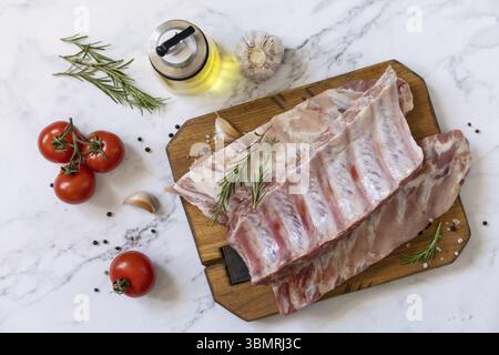 Rohe Kalbsbrust Rippchen Fleisch mit Gemüse und Gewürzen auf kurzen Ersatzrippchen zum Kochen auf Marmorplatte. Draufsicht, flach Stockfoto