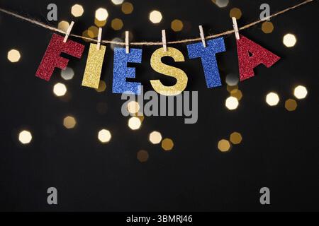 Fiesta-Wort aus glänzendem Papier und Nadeln auf schwarzem Hintergrund und Bokeh-Lichtern. Cinco de Mayo Konzept Stockfoto