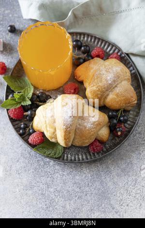 Leckere frisch gebackene Croissants und Orangensaft auf grauem Stein Hintergrund, Frühstückskonzept. Dessert französisches Gebäck Stockfoto