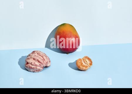 Zusammensetzung von frischen Früchten, Mango und Mandarine, Hälfte geschälter Mandarine und Mango auf blauem Hintergrund. Nachgeahmtes, zweifarbiges Pastellfarben Stockfoto