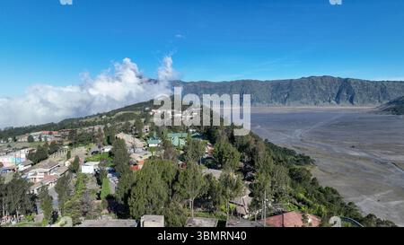 Dieser Blick aus der Vogelperspektive auf Cemoro Lawang fängt das Dorf ein, das über dem riesigen Sandmeer thront, mit den Caldera-Wänden, die eine atemberaubende Natur schaffen Stockfoto