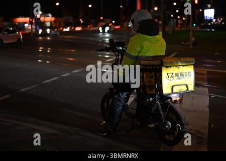 Rückansicht eines Mitarbeiters, der nachts an einer Kreuzung wartet, mit beleuchtetem Hungry Panda Container auf der Rückseite ihres Rollers Stockfoto