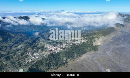 Das Dorf Cemoro Lawang liegt am üppigen Rand der Caldera, umgeben von sanften grünen Hügeln und vor einem dramatischen Wolkenmeer im Stockfoto