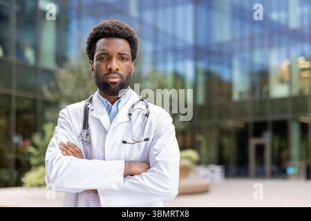 Ein selbstbewusster Arzt steht draußen, Arme gekreuzt, mit einem Stethoskop um den Hals, bereit, medizinische Hilfe zu leisten. Stockfoto