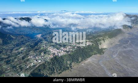 Das Dorf Cemoro Lawang liegt am üppigen Rand der Caldera, umgeben von sanften grünen Hügeln und vor einem dramatischen Wolkenmeer im Stockfoto