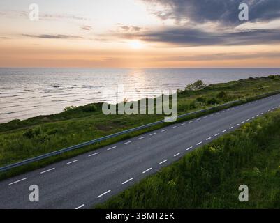 Aus der Vogelperspektive einer malerischen Autobahn entlang der Ostseeküste in Estland bei Sonnenuntergang. Die perfekte Straße für einen Roadtrip im Sommer. Stockfoto